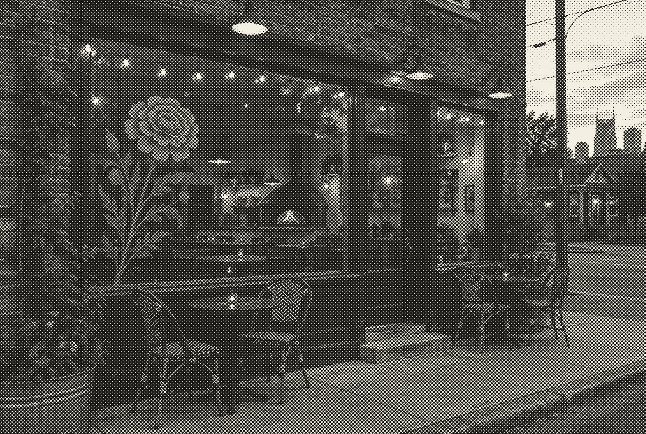 The pizzeria storefront at dusk with a marigold painted on the window